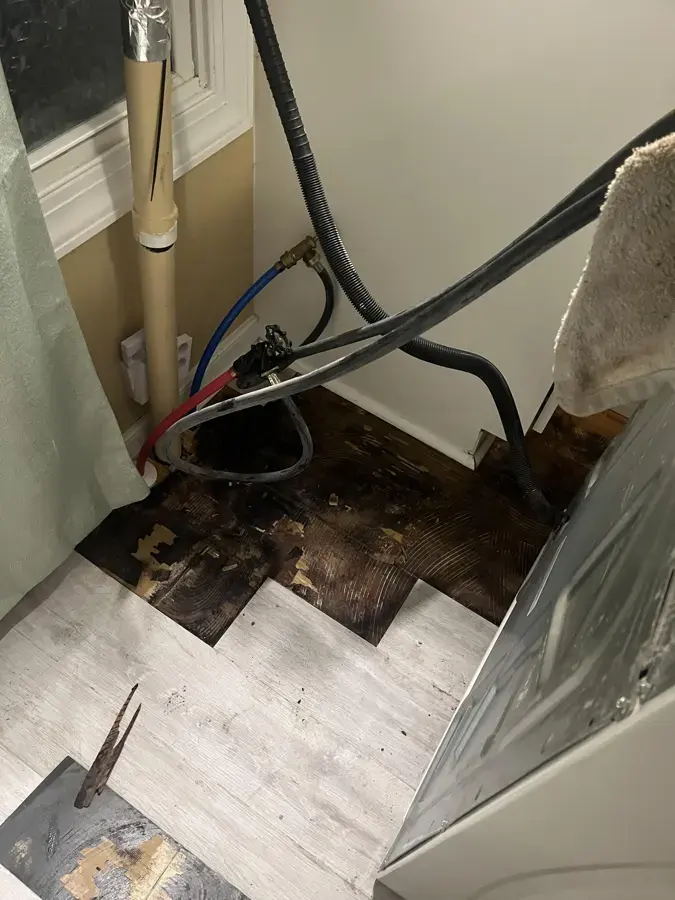 Water-damaged floor exposed behind a washer after a supply hose leak