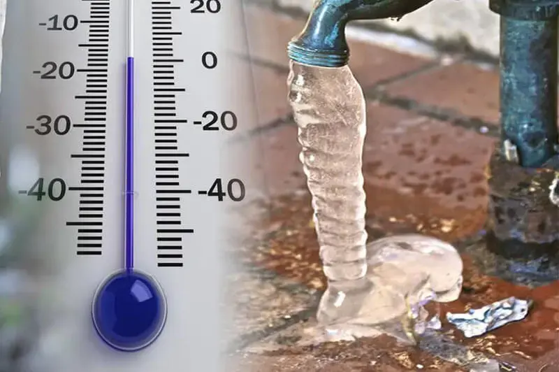 Frozen outdoor hose bib encased in ice beside a thermometer below zero